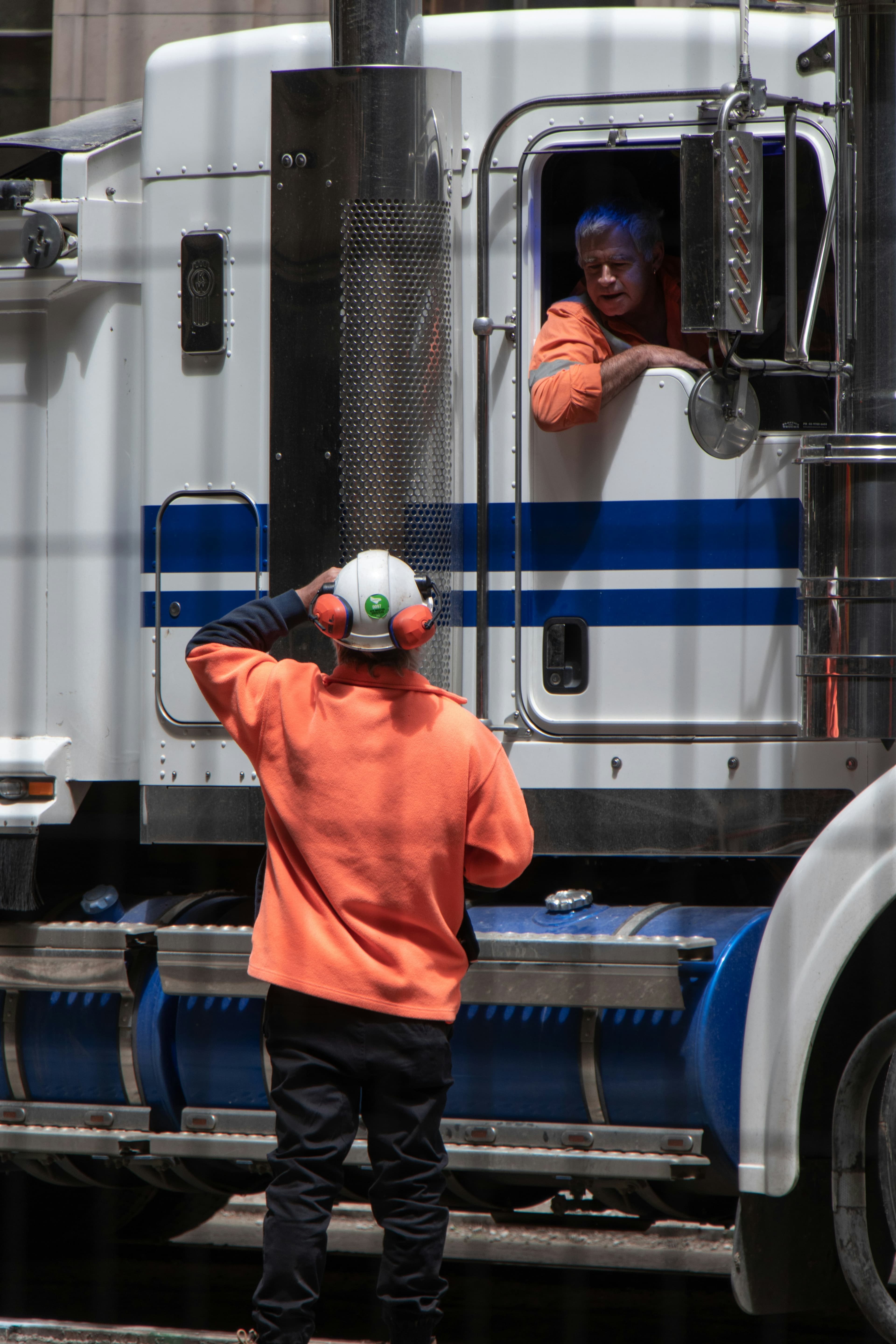 Two truck drivers in orange vests speaking next to a semi truck